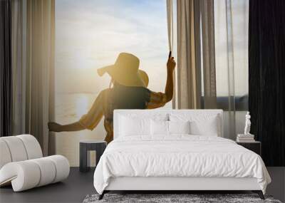 Rear back view woman opening curtains, relaxing and looking beautiful seascape panorama with rays of sun light in holiday on the balcony in high quality hotel feeling happy. Composition of nature Wall mural