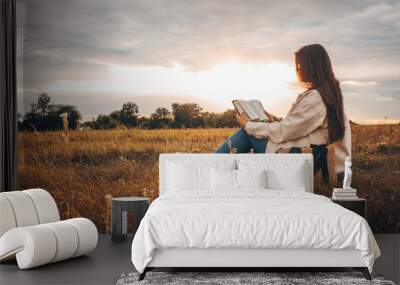 Christian woman holds bible in her hands. Reading the Holy Bible in a field during beautiful sunset. Concept for faith, spirituality and religion. Peace, hope Wall mural