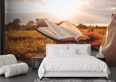 Christian woman holds bible in her hands. Reading the Holy Bible in a field during beautiful sunset. Concept for faith, spirituality and religion. Peace, hope Wall mural