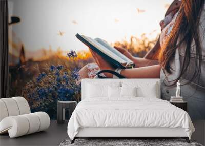 Christian woman holds bible in her hands. Reading the Holy Bible in a field during beautiful sunset. Concept for faith, spirituality and religion. Peace, hope Wall mural