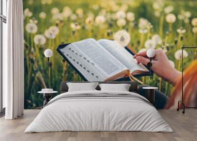 Christian woman holds bible in her hands. Reading the Holy Bible in a field during beautiful sunset. Concept for faith, spirituality and religion. Peace, hope Wall mural