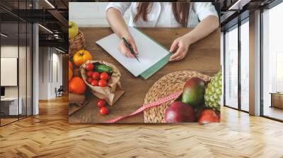 Doctor nutritionist writing case history in the office. Young woman dietitian prescribing recipe Wall mural