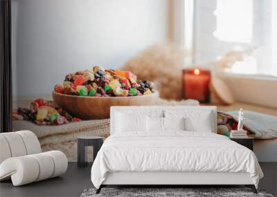 Wooden plate with candied fruits and dried fruits on a wicker stand against the background of a candle, eco concept Wall mural