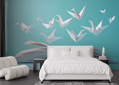 A group of white paper cranes, a symbol of peace and hope, fly out of an open book against a light blue background. Wall mural