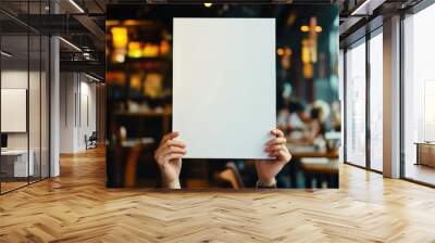 A person holds a blank white sign in front of them, with a blurred cafe background. Wall mural