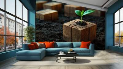 A small green plant sprout growing up from a wooden block with a blurred background of other wooden blocks in fertile soil. Wall mural