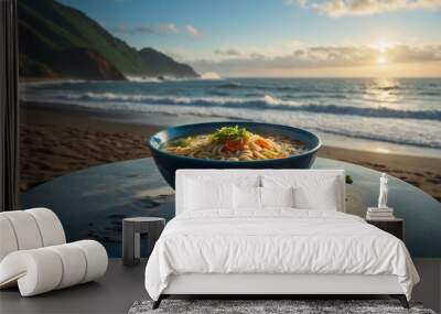 Steaming bowl of noodle soup, set on a table with a view of the ocean waves gently crashing on the shore. Wall mural