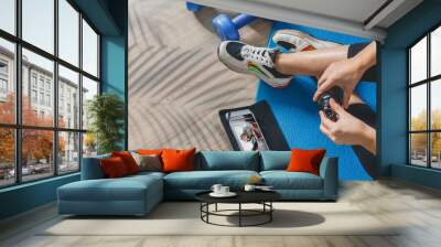 Fitness at home, remote training with virtual instructor. Woman in sportswear sitting on the floor with dumbbells laptop at home. Sports and recreation concept in lockdown with fitness apps online Wall mural