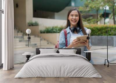 Beautiful student asian woman with backpack and books outdoor. Smile girl happy carrying a lot of book in college campus. Portrait female on international Asia University. Education, study, school Wall mural