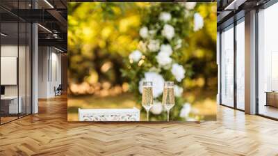 two glasses of champagne stand on a table against the backdrop of a wedding arch. Wall mural