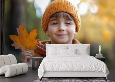 Handsome cute 7 years old boy in the fall season autumn landscape sunny day, trees and leaves background, holding colorful maple leaf Wall mural