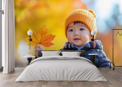 Handsome cute asian baby boy in the fall season autumn landscape sunny day, trees and leaves background, holding colorful maple leaf Wall mural