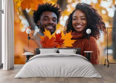 Handsome lovely african woman and man couple in the fall season autumn landscape sunny day, trees and leaves background, holding colorful maple leafs Wall mural