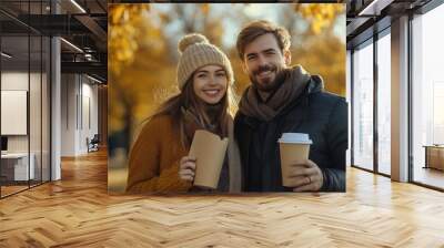 Handsome lovely woman and man couple in the fall season autumn landscape sunny day, trees and leaves background, holding hot paper glass with coffee Wall mural