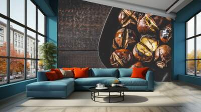 Roasted edible chestnuts in cast iron skillet over rustic wooden table. Wall mural