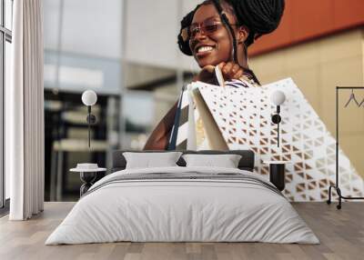 African American woman wearing glasses, with shopping bags, woman with bags coming out of the store Wall mural