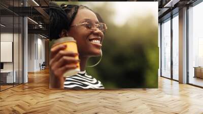 african young woman, wearing sunglasses, holds coffee in takeaway glass Wall mural