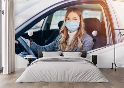 Beautiful young girl in a mask sitting in a car, protective mask against coronavirus, driver on a city street during a coronavirus outbreak Wall mural