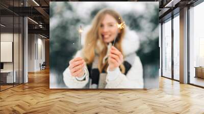 Charming woman in warm winter clothes posing with sparklers on the street in winter Wall mural