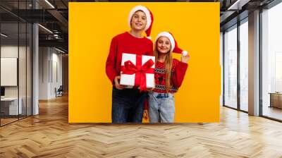 Christmas two friends, a boy and a girl in santa claus hats and gifts, on a yellow background. christmas eve new year Wall mural