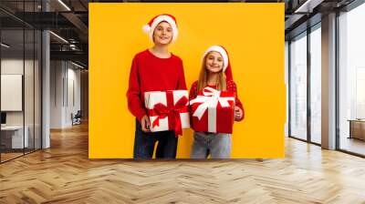 Christmas two friends, a boy and a girl in santa claus hats and gifts, on a yellow background. christmas eve new year Wall mural