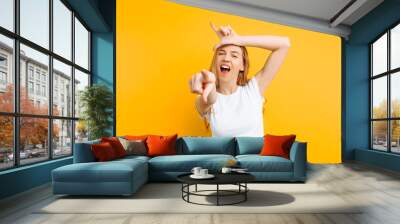 girl shows the gesture of a loser or loser, in a white t-shirt with a grin on his face, on a yellow background Wall mural