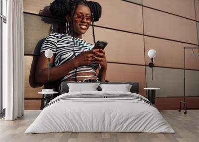 Happy African American woman using mobile phone over brown background Wall mural