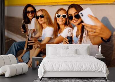 Happy young people with drinks have fun, spend time together and take a selfie on a mobile phone, against the background of a yellow wall on a summer sunny day Wall mural