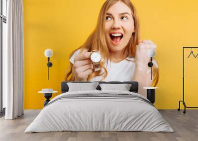 Portrait of a positive young woman, pointing her finger at the clock, on a yellow background Wall mural