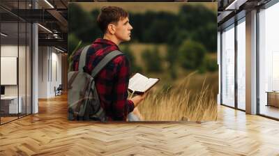 Reading the Bible outdoors in nature. A man in sunglasses and a shlap holds a Bible in his hands Wall mural