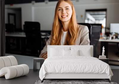 Smiling business young woman sitting at work desk in office Wall mural