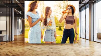 Three women in summer clothes and hats. Carefree women have a picnic on the street. Positive girls drinking drinks Wall mural