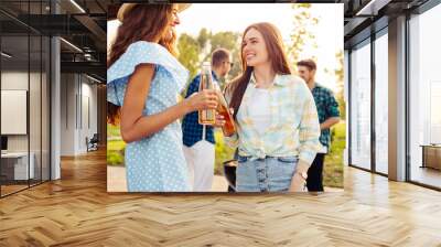 Two girls are drinking drinks, in the background a group of friends having fun grilling meat enjoying barbecue Wall mural