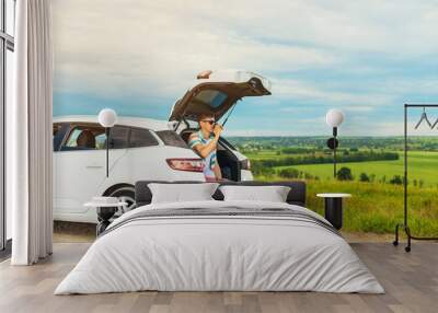 young male traveler sitting in the trunk of his car, man having a rest during a trip, outdoors with a beautiful landscape, travel Wall mural