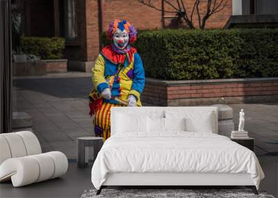 Angry clown is sitting in the middle of the city. He is waiting to play. He is holding a weapon in his hands. Wall mural