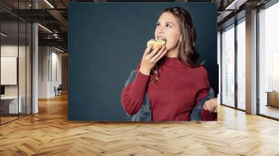 tasty bite in donut - teen girl eats a sweet fried delicious doughnut and look up to upper corner with left copy space Wall mural