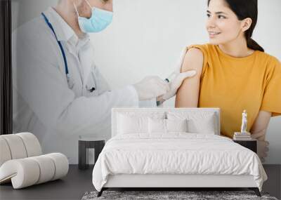 a doctor in a medical mask and a dressing gown seals an injection on a woman's shoulder with adhesive plaster covid Wall mural