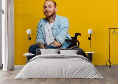 A man in a wheelchair smile and happiness, thumb up, with tattoos on his hands sits on a yellow studio background, the concept of health a person with disabilities Wall mural