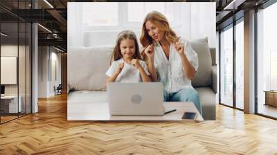 A mother and her daughter enjoy a moment of success and joy together at their home, using a laptop Wall mural