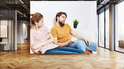 A woman in a striped T-shirt and a man on the couch watching the TV in a bright room Wall mural