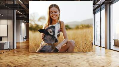 A woman strokes and hugs a husky dog ​​and smiles outside the house in nature in a field in autumn at sunset. Lifestyle with an animal friend Wall mural