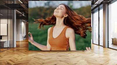 A young woman laughing and smiling merrily in nature in the park with the sunset lighting illuminating her long red hair Wall mural