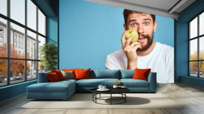 An energetic man with a green apple on a blue background gestures with his hands Copy Space emotions Wall mural