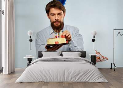 Bearded man with a plate of cake on a blue background and a birthday party hat on his head Wall mural