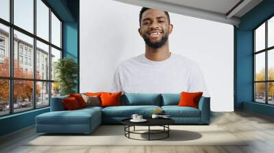 Confident young african american man smiling and standing casually against a plain white background in casual attire Wall mural