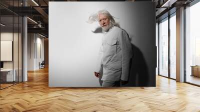 Elderly man with long white hair wearing a white jacket against a soft gray background, showcasing a contemplative and artistic pose Wall mural