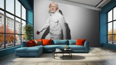 Elderly man with long white hair wearing a white jacket poses confidently on a minimalist grey background, showcasing modern fashion and timeless style, embodying elegance Wall mural