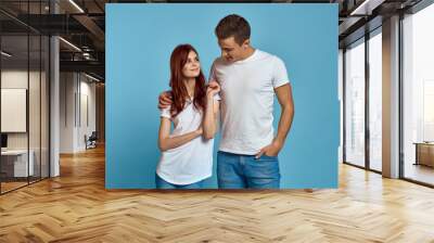 enamored man and woman in jeans and a T-shirt on a blue background hug each other and have fun Wall mural