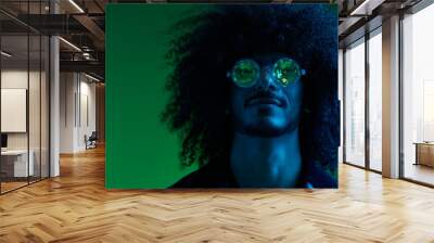 Fashion portrait of a man with curly hair on a green background with sunglasses, multinational, colored pink light, trendy, modern concept. Wall mural