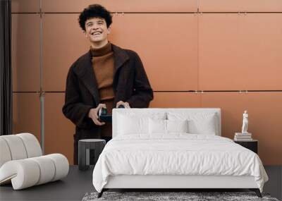 Fashion portrait of a young man in a coat holding a remote control in front of an orange wall Wall mural